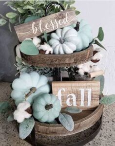 a three tiered basket filled with pumpkins and greenery next to a sign