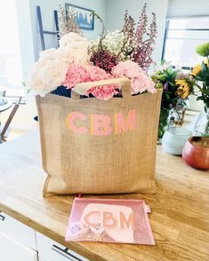 a bag sitting on top of a wooden table with flowers in the front and behind it