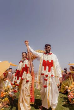 two people dressed in white and red standing next to each other with flowers on them