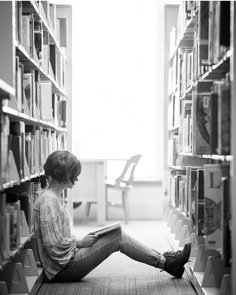 a woman is sitting on the floor in front of a book shelf with many books