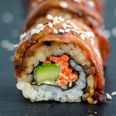 a sushi roll with vegetables and sauce on it sitting on a black surface next to sesame seeds