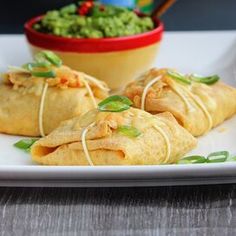 some food is on a white plate with a bowl of guacamole in the background