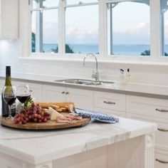 a wine bottle, cheese and grapes on a cutting board sitting on a kitchen counter