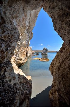 the view from inside a cave looking out at water and rocks in the distance, with blue sky above