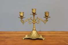 a golden candelabra with three candles on it sitting on a wooden table