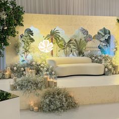 a white couch sitting on top of a stage surrounded by trees and candles in front of a wall