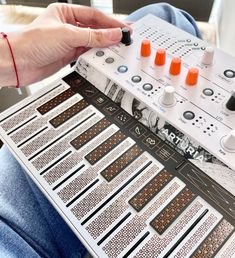 a person is sitting down and playing an electronic music board with orange knobs on it