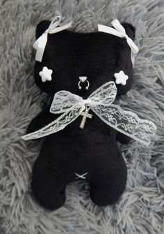 a black teddy bear sitting on top of a fluffy gray carpet with a white ribbon around it's neck