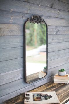 a mirror hanging on the side of a wooden wall next to a book and plant