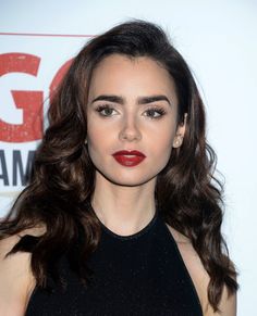 a woman with long dark hair wearing a black dress and red lipstick is posing for the camera