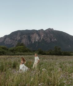 a man and woman standing in a field with mountains in the background