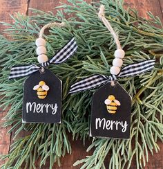 two christmas tags with the words merry and a bee on them hanging from pine branches