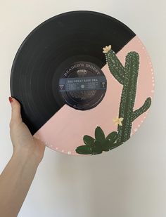 a person holding up a record with a cactus on the side and pink, black, and white background