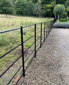 a black metal fence in the middle of a gravel path with grass and bushes behind it