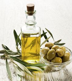 an olive oil bottle next to a glass bowl filled with green olives