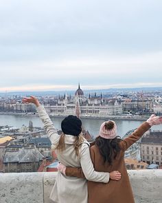 two women standing on top of a building with their arms in the air and looking out over a city