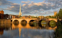 a bridge over a body of water with buildings on the other side and a church steeple in the background