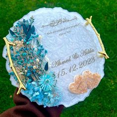 a person holding up a plaque with flowers on it in front of some green grass