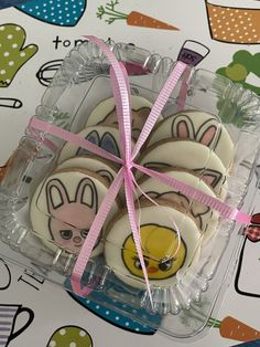 some cookies are in a plastic box with pink ribbon on it and bunny ears painted on them