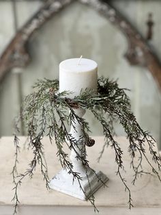 a white candle sitting on top of a wooden table next to a wreath and pine cones