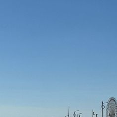 an airplane is flying in the sky over a pier and ferris wheel on a sunny day