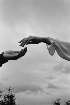 two hands reaching out towards each other in front of a sky with clouds and trees