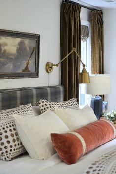 a bed with white and orange pillows in a bedroom next to a painting on the wall