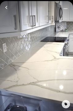 a kitchen with white cabinets and marble counter tops