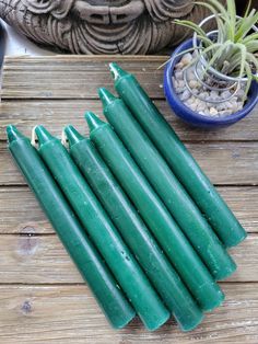 several green candles sitting on top of a wooden table next to a potted plant