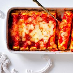 a square casserole dish with cheese and sauce in it, next to a spoon