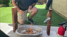 a man kneeling down in front of a fire pit on a table with a bottle of ketchup next to it