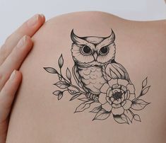 an owl tattoo on the back of a woman's shoulder with flowers around it