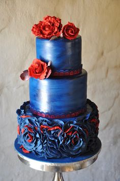 a three tiered blue cake with red roses on top is sitting on a silver plate