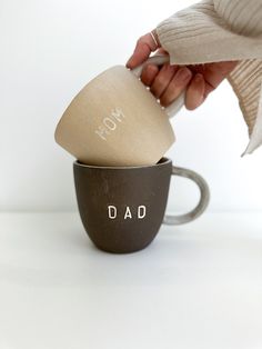 a woman is holding a coffee mug with the word dad printed on it, while another cup has its lid open