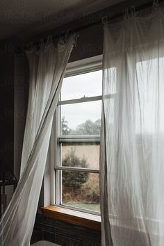 an open window with white curtains in a dark room