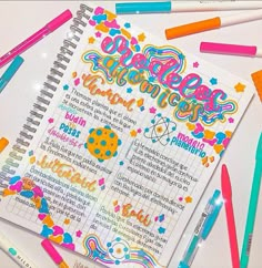 an open notebook surrounded by markers and pens