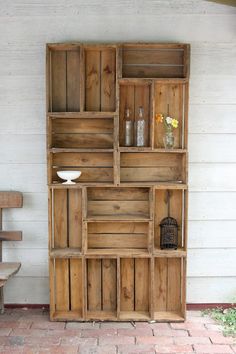 a wooden shelf sitting on top of a brick floor next to a white wall with flowers in vases