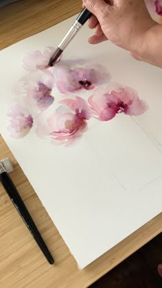 a person is painting flowers on a piece of paper with watercolors and a brush