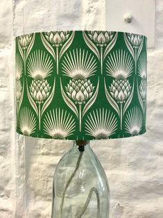 a lamp that is sitting on a table next to a white wall with a green lampshade