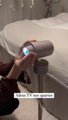 a person holding a camera in front of a bed with white sheets and string lights