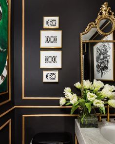 a bathroom with black walls and white flowers in a vase on the sink counter next to it