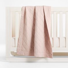 a baby crib with a pink blanket hanging from it's side, and a white crib in the background