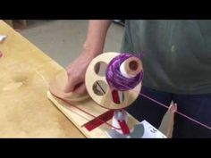 a person is working with some yarn on a wooden board and thread spools are in the background