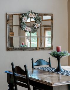 a dining room table and chairs with a mirror on the wall above it that is decorated with flowers