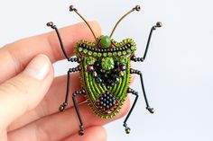 a hand holding a green beaded insect