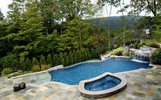 an outdoor swimming pool surrounded by trees and rocks with a waterfall in the middle that is built into the ground