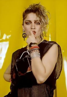 a woman standing in front of a yellow wall with her hand on her mouth and wearing bracelets