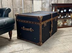 an old trunk sitting in front of a leather chair and shelf with bottles on it