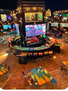 an outdoor bar with tables and chairs around it, lit up by colorful lights at night