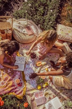 three women are sitting on a blanket in the middle of a garden and looking at papers